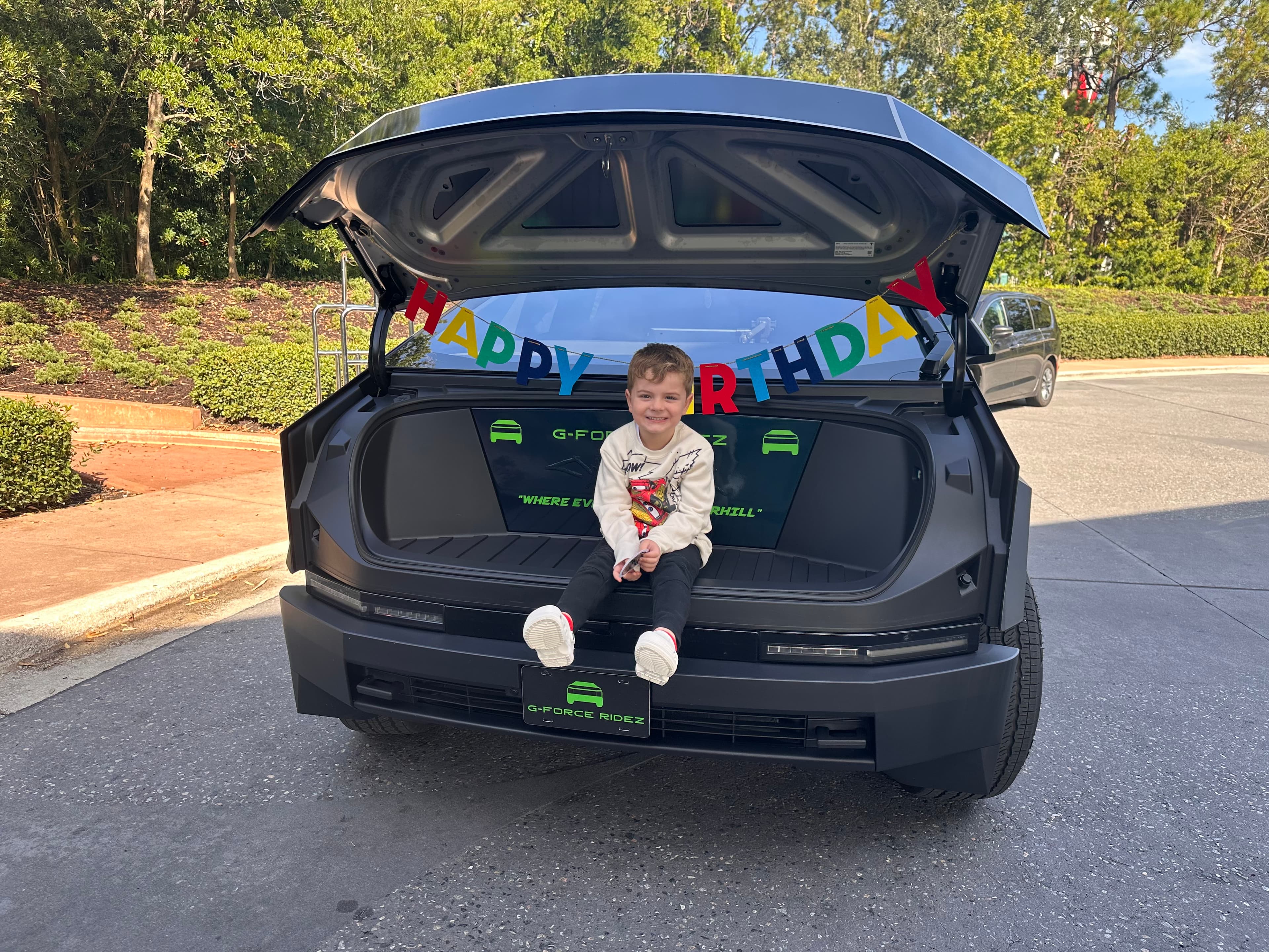 Birthday kid sitting in the Cybertruck trunk with Happy Birthday banner